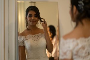 Bride in lace wedding dress admiring her reflection in a mirror indoors.