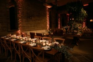 Warmly lit dining set-up in a decorated event hall with flowers and candles.